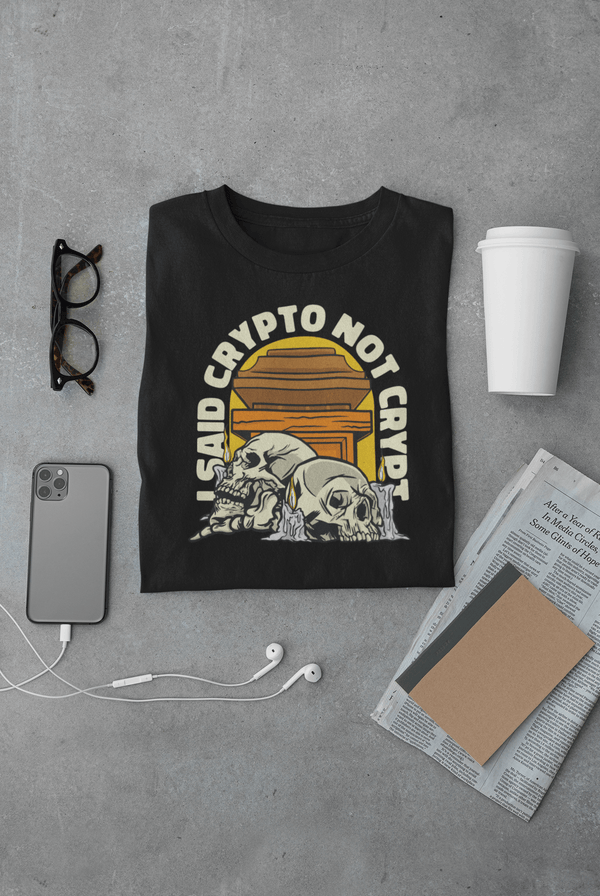 Black Crypt Tshirt with "I Said Crypto Not Crypt" text, skeleton graphic, folded on gray surface with smartphone, glasses, cup, newspaper